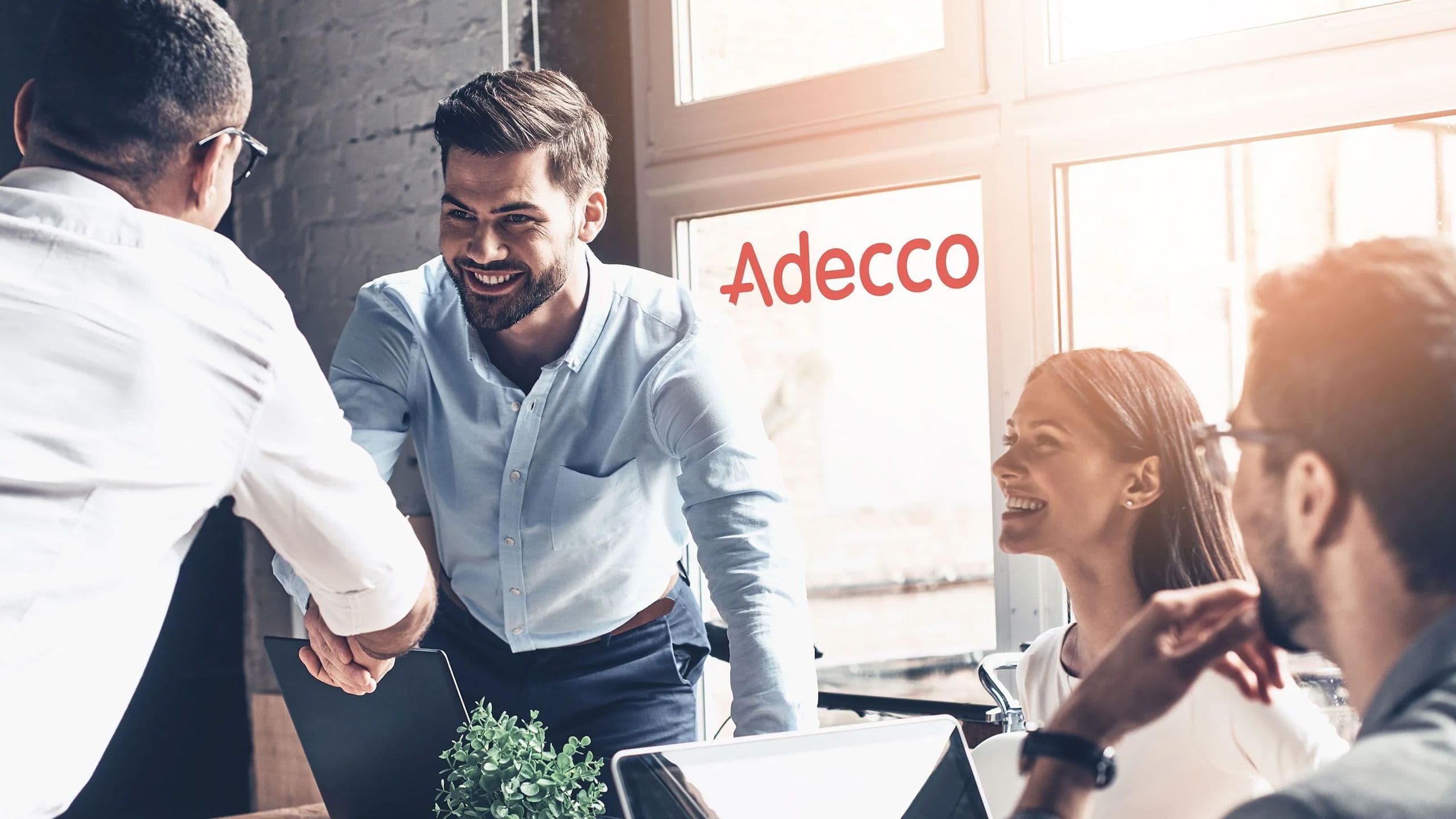 Fototermin bei Adecco: 1 Kollege posiert mit seinen beiden Kolleginnen am Hochtisch im Büro.